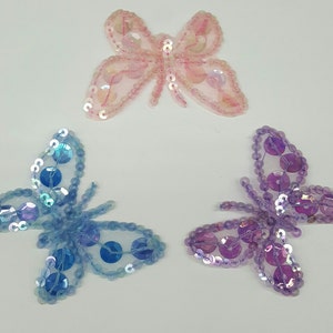 以下が含まれることがあります： 3つの虹色の蝶のアップリケ。1つはピンク、1つはブルー、もう1つはパープルです。