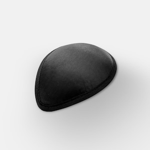 May include: A black eye patch, teardrop-shaped, with a black trim. The patch is made of a soft, matte material and is designed to cover one eye. The background is plain white.