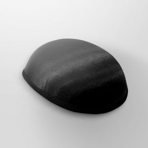 May include: A black satin kippah, a traditional Jewish head covering. The kippah is oval-shaped with a black trim around the edge. The fabric has a subtle sheen, and the kippah is set against a white background.