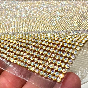 May include: A sheet of gold-toned rhinestone mesh fabric. The rhinestones are clear with a rainbow iridescent finish. The mesh is flexible and can be used for a variety of craft projects.