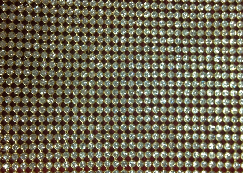 May include: A close-up of a gold mesh fabric with small, clear rhinestones. The rhinestones are arranged in a grid pattern.