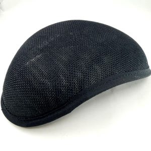 Puede incluir: Gorra de estilo newsboy de malla negra. La gorra tiene una corona redondeada y una visera pequeña y rígida. El material de malla permite la transpiración. La gorra es de color negro liso y parece estar hecha de una tela ligera.