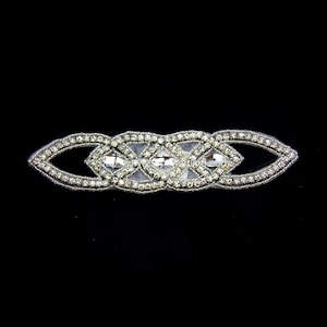 May include: Silver rhinestone trim with a geometric design. The trim features a series of interlocking ovals and diamonds, all set with clear rhinestones.