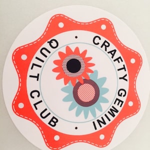 Puede incluir: Una pegatina circular roja y blanca con forma de estrella. La pegatina tiene el texto "Crafty Gemini Quilt Club" escrito alrededor del borde. El centro de la pegatina presenta dos flores estilizadas.