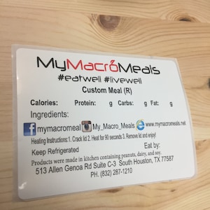 May include: A white label with the text "MyMacroMeals #eatwell #livewell Custom Meal (R)" and information about calories, protein, carbohydrates, and fat.  The label also includes social media icons for Facebook, Instagram, and a website.  The label includes instructions for heating the meal, a note to keep it refrigerated, and an expiry date.  The label also includes the address and phone number for the company.