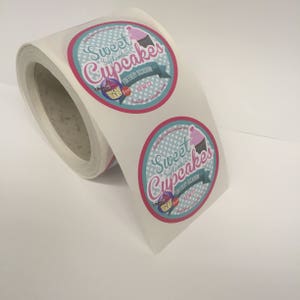 May include: Roll of white sticker labels with a pink and blue design. The labels feature a cupcake with the text "Sweet September Cupcakes" and "For Every Occasion".