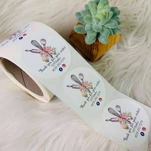 Op de afbeelding: Ronde witte sticker met een bloemmotief en een deegroller, garde en lepel. De sticker zegt "Bedankt voor uw bestelling! 559 Bakery #559-392-7279" en heeft social media-iconen voor Facebook en Instagram.