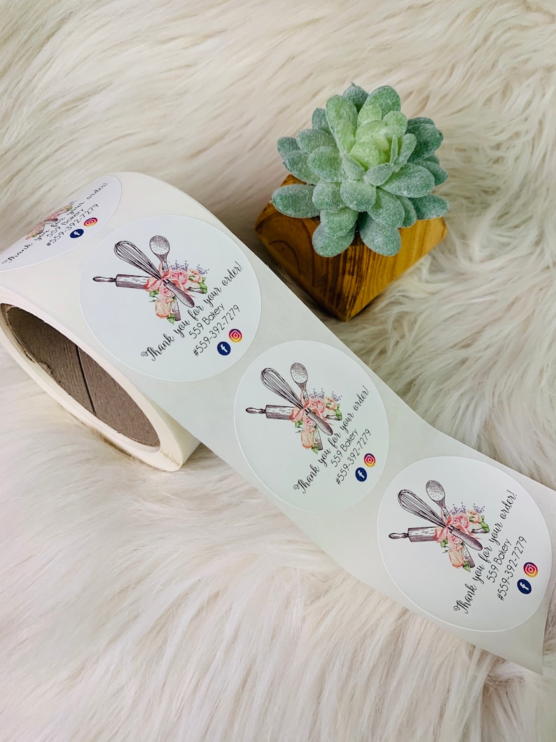 Op de afbeelding: Ronde witte sticker met een bloemmotief en een deegroller, garde en lepel. De sticker zegt "Bedankt voor uw bestelling! 559 Bakery #559-392-7279" en heeft social media-iconen voor Facebook en Instagram.