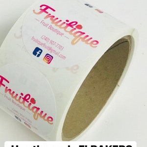Puede incluir: Un rollo de pegatinas redondas con el logotipo "Fruitique - Fruit Boutique" y la informaci&oacute;n de contacto. El texto "Use the code FLBAKERS and save 15% off on the website swipe up to shop" se muestra debajo del rollo de pegatinas.