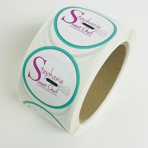 Puede incluir: Rollo de pegatinas redondas con borde turquesa y fondo blanco. Las pegatinas presentan una gran letra rosa "S" y el texto "Stephanie Sweet Chef" con un batidor negro.