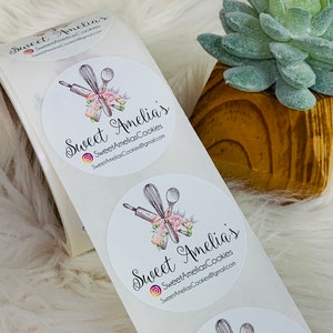 Op de afbeelding: Drie witte ronde stickers met een bloemmotief en de tekst "Sweet Amelia's" en "SweetAmeliasCookies@gmail.com".