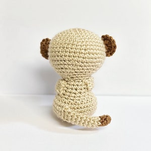 May include: A crocheted meerkat toy with a beige body, brown ears, and a brown tail.