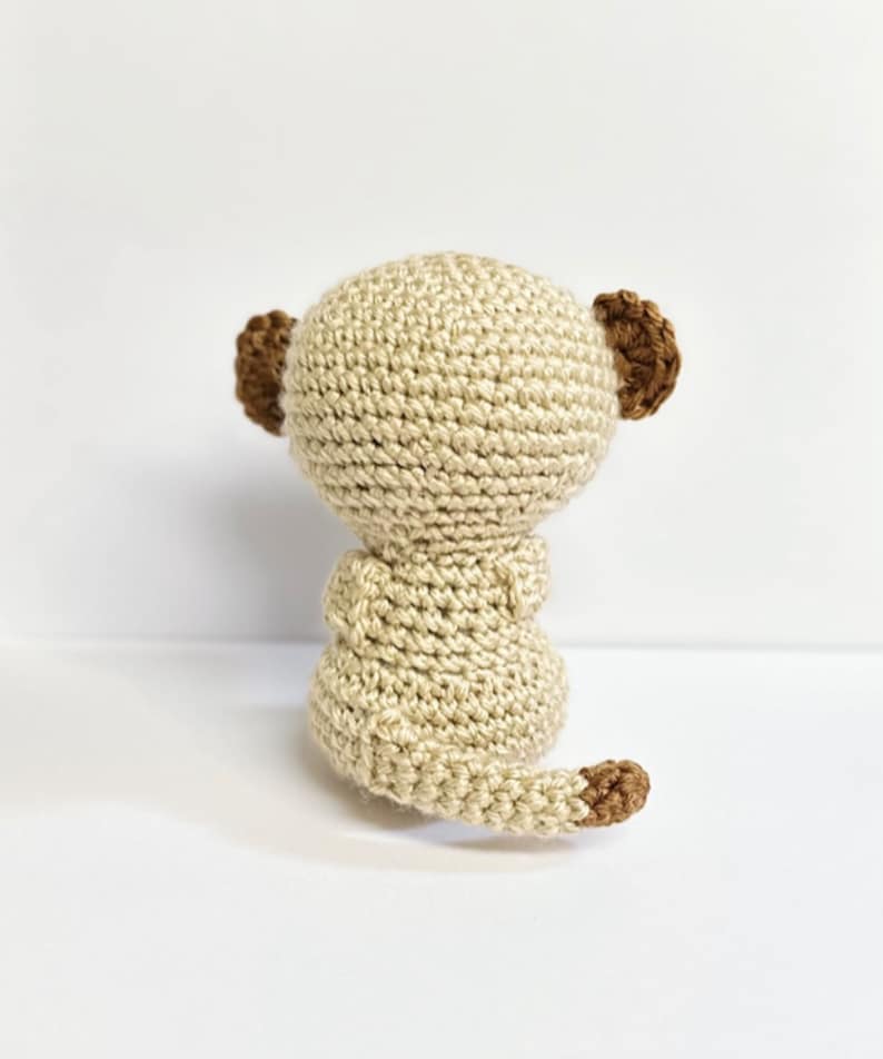 May include: A crocheted meerkat toy with a beige body, brown ears, and a brown tail.