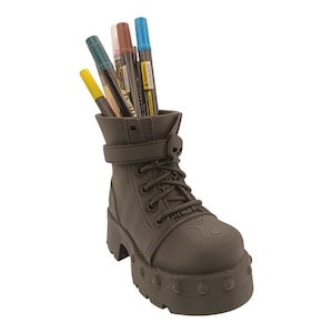 May include: A dark brown boot-shaped desk organizer with a skull accent on the strap. The organizer holds several colorful markers and pens. The boot has a chunky sole and detailed lacing.