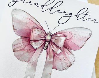 May include: A white greeting card featuring a watercolor illustration of a pink butterfly with a central bow and small clear gems. The text "Granddaughter" is written in black script at the top, and "HAPPY BIRTHDAY LAUREN" is printed in black at the bottom.
