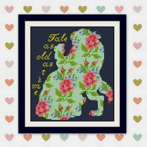 May include: Cross-stitch art in a black frame. The design features a silhouette filled with floral patterns of pink roses and blue accents. The words "Tale as old as time" are written in gold.