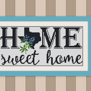 May include: A framed cross-stitch design with the text "HOME" with the state of Texas in the "O" and the text "sweet home" below. The design is in black and white with a blue flower.