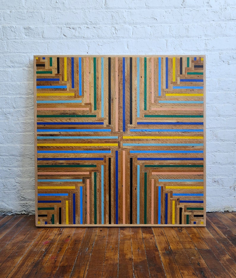 Front view of reclaimed wood lath table top in colorful geometric stripe pattern. Shown against white brick wall.