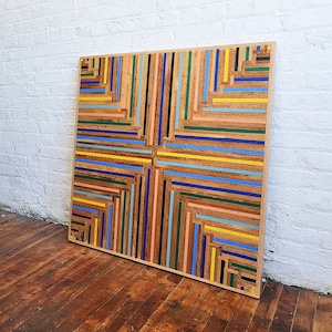Reclaimed wood lath table top in colorful geometric stripe pattern. Shown against white brick wall.
