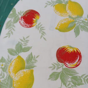 Könnte beinhalten: Weißes Tischtuch mit einem sich wiederholenden Muster aus roten Äpfeln und gelben Zitronen. Die Früchte sind von grünen Blättern und kleinen weißen Blüten umgeben. Das Design ist im Vintage-Stil.