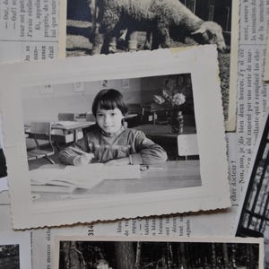 Puede incluir: Foto en blanco y negro de una ni&ntilde;a sentada en un escritorio en un aula. Lleva una camisa de color claro y tiene el pelo recogido hacia atr&aacute;s. Est&aacute; mirando un libro delante de ella.