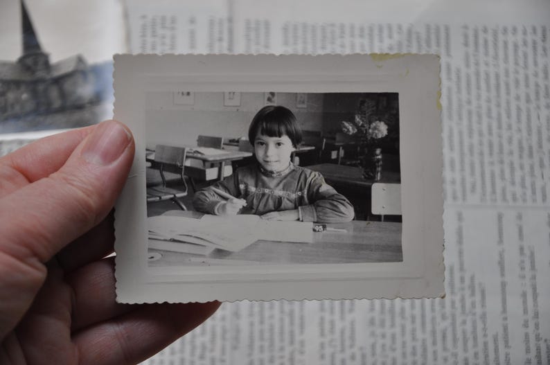 Puede incluir: Una ni&ntilde;a joven con cabello oscuro se sienta en una mesa en un aula. Lleva un su&eacute;ter de color claro y mira un libro. La mesa est&aacute; cubierta de papeles y libros.