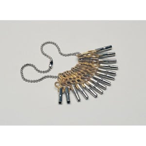 May include: A set of silver and gold-toned keys attached to a silver ball chain. The keys are arranged in a fan shape, with a mix of silver and gold metal. The background is plain white.