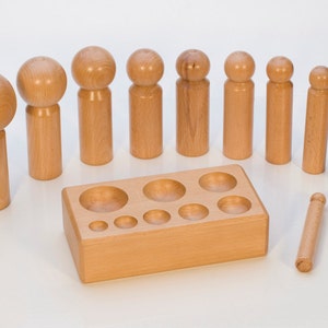 May include: A set of wooden dowels of varying sizes, with rounded tops, and a wooden base with circular cutouts. The dowels are designed to fit into the corresponding cutouts in the base.