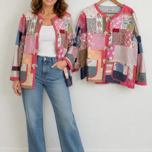Puede incluir: Chaqueta patchwork con ribete rosa y cierres de palanca. La chaqueta presenta una variedad de patrones de tela en tonos rosa, azul y beige. La modelo lleva la chaqueta con vaqueros azules y zapatillas blancas.