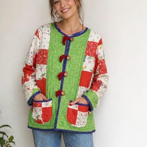 May include: A patchwork jacket with a green central panel and red, white, and floral patterned sleeves. The jacket has a blue trim, wooden buttons, and red bows. It features two front pockets.