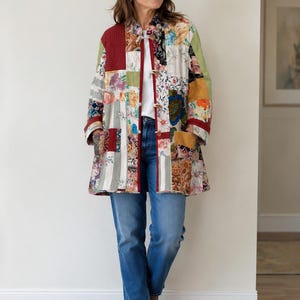 Peut inclure: Un manteau patchwork coloré avec des motifs floraux et géométriques dans les tons de rouge, vert, jaune et bleu. Le manteau a une fermeture à boutons et est porté avec un jean bleu et des bottines marron. Le design du manteau rappelle un patchwork.