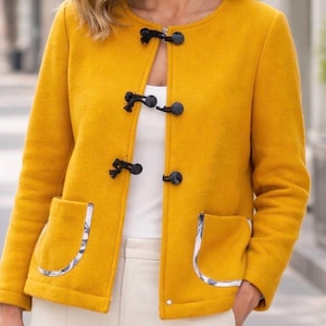 Puede incluir: Chaqueta amarillo mostaza con cierres de palanca negros y dos bolsillos delanteros. Los bolsillos están ribeteados con una tela estampada. La chaqueta tiene mangas largas y cuello redondo.