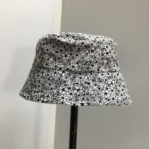 May include: A white bucket hat with a black floral print. The hat is made of a lightweight fabric and has a wide brim.