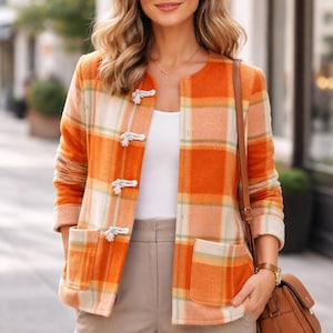 May include: An orange and cream plaid jacket with three toggle closures and two front pockets. The jacket is paired with beige pants and a brown purse. The outfit is completed with a gold watch.