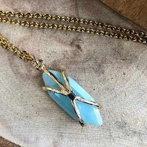 May include: A gold chain necklace with a light blue gemstone pendant. The pendant is wrapped in a gold wire design.