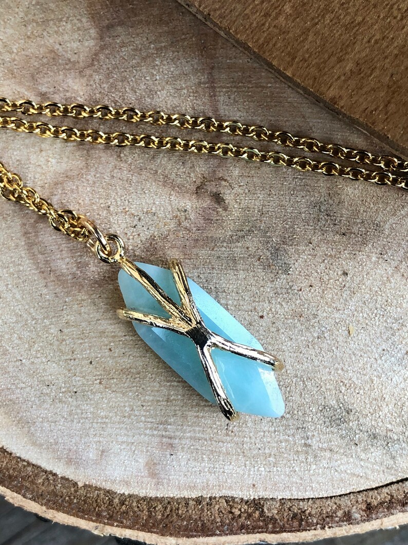 May include: A gold chain necklace with a light blue gemstone pendant. The pendant is wrapped in a gold wire design.