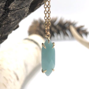 May include: A delicate gold chain necklace with a light blue gemstone pendant. The pendant is a marquise shape with gold accents.