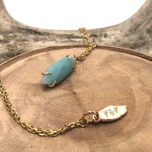 May include: A gold chain necklace with a light blue gemstone pendant and a gold leaf charm with the inscription "T&F".