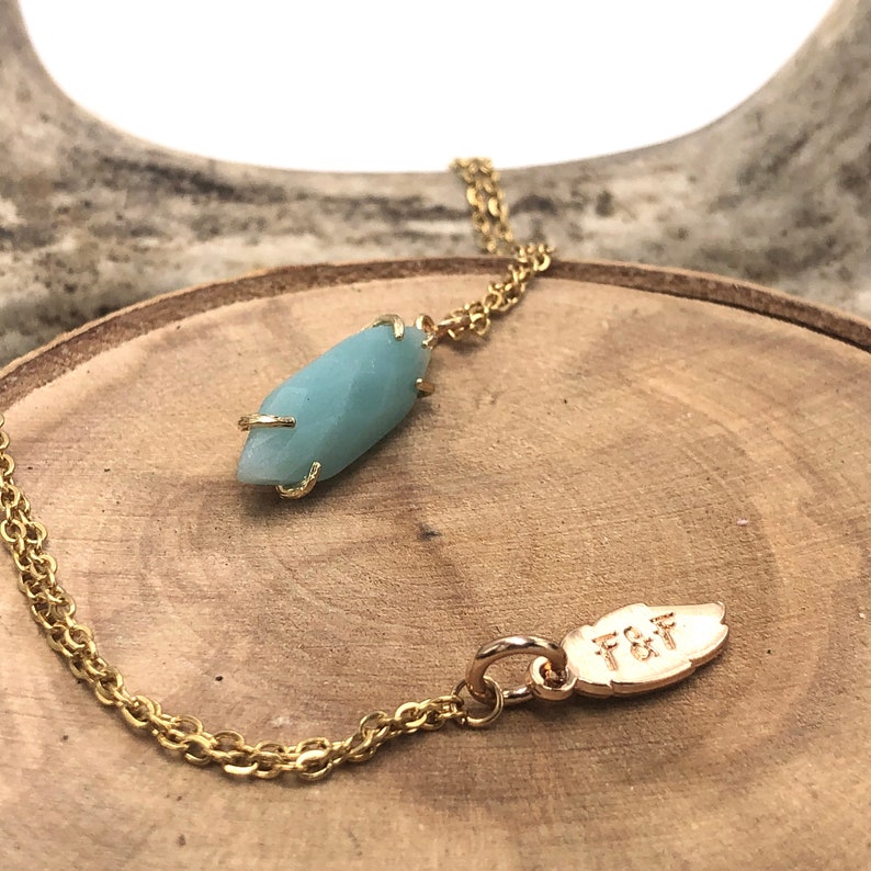 May include: A gold chain necklace with a light blue gemstone pendant and a gold leaf charm with the inscription "T&F".