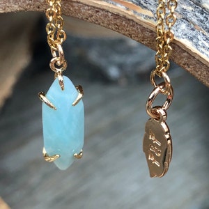 May include: A gold chain necklace with a light blue aquamarine crystal pendant and a gold tag with the text "4711" on it.