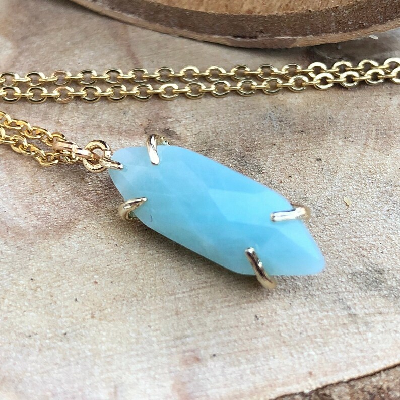May include: A gold chain necklace with a light blue gemstone pendant. The pendant is a faceted, elongated shape with gold accents.