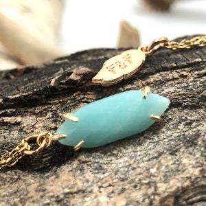 May include: A gold chain necklace with a light blue gemstone pendant and a gold leaf charm with the inscription "F&F".