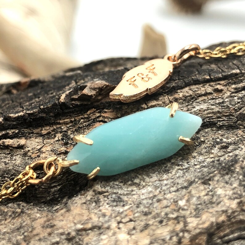 May include: A gold chain necklace with a light blue gemstone pendant and a gold leaf charm with the inscription "F&F".
