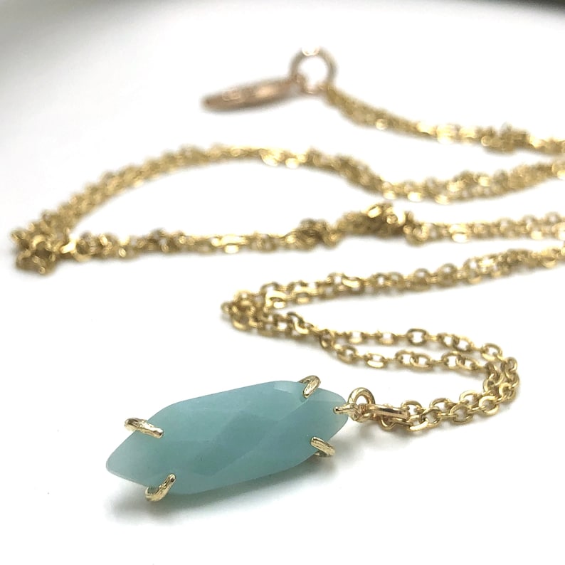 May include: A gold chain necklace with a light blue gemstone pendant. The pendant is faceted and has a gold setting.