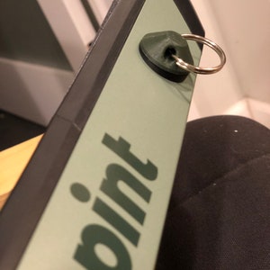 May include: A close-up of a green and black pint glass with a metal ring attached. The glass has the word "pint" printed on it in a dark green colour.