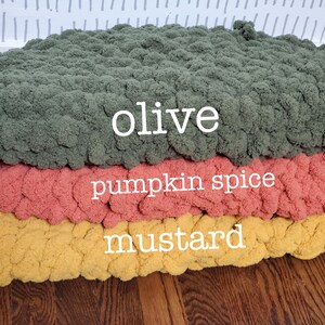 Pu&ograve; includere: Tre pouf rotondi in maglia di colore oliva, spezie di zucca e senape. I pouf sono impilati uno sopra l'altro.