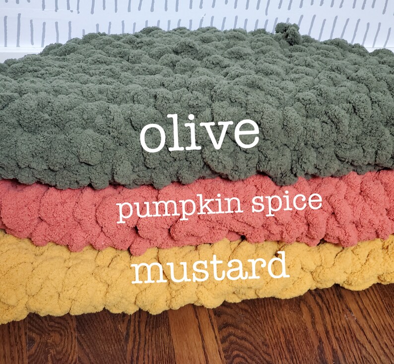 Pu&ograve; includere: Tre pouf rotondi in maglia di colore oliva, spezie di zucca e senape. I pouf sono impilati uno sopra l'altro.