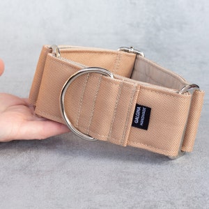 Może przedstawiać: Beżowy obroża dla psa ze srebrnymi okuciami. Obroża wykonana jest z grubego, wytrzymałego materiału i ma etykietę z napisem "Galgina Handmade".