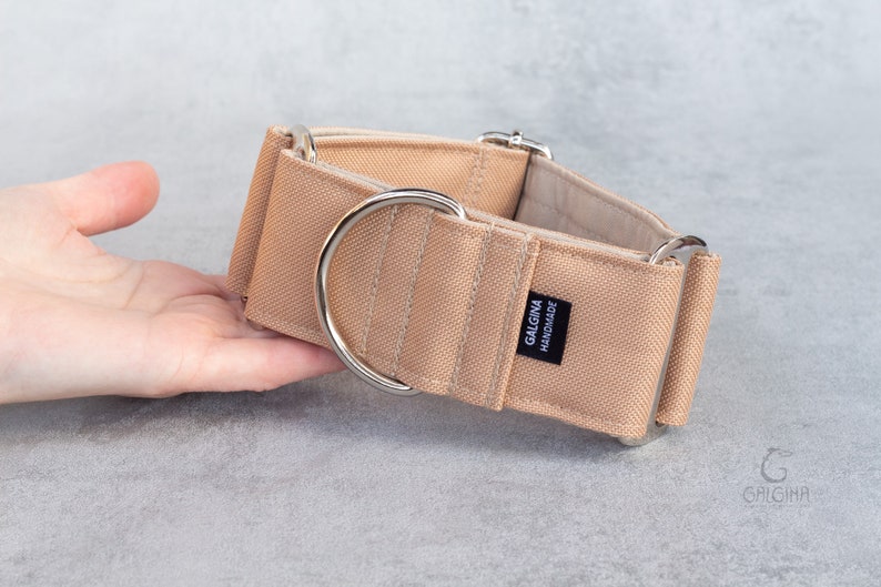 Może przedstawiać: Beżowy obroża dla psa ze srebrnymi okuciami. Obroża wykonana jest z grubego, wytrzymałego materiału i ma etykietę z napisem "Galgina Handmade".