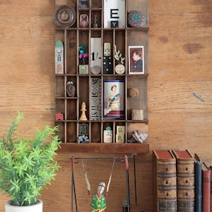 May include: A wooden printer's tray displaying a collection of miniature items, such as a clock, a small owl, and a portrait. A toy swing and several antique books are also present, creating a vintage aesthetic.